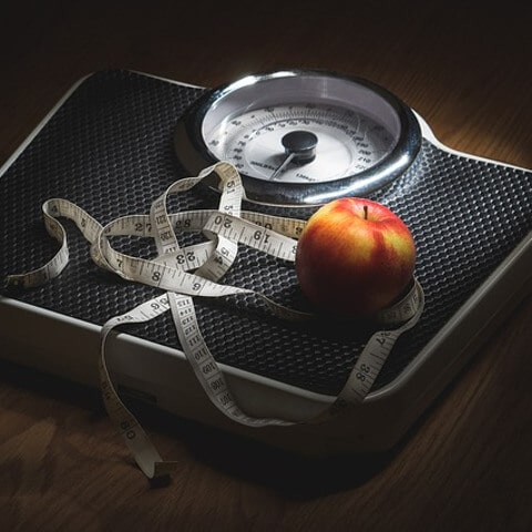 An apple and a metre tape on a scale.