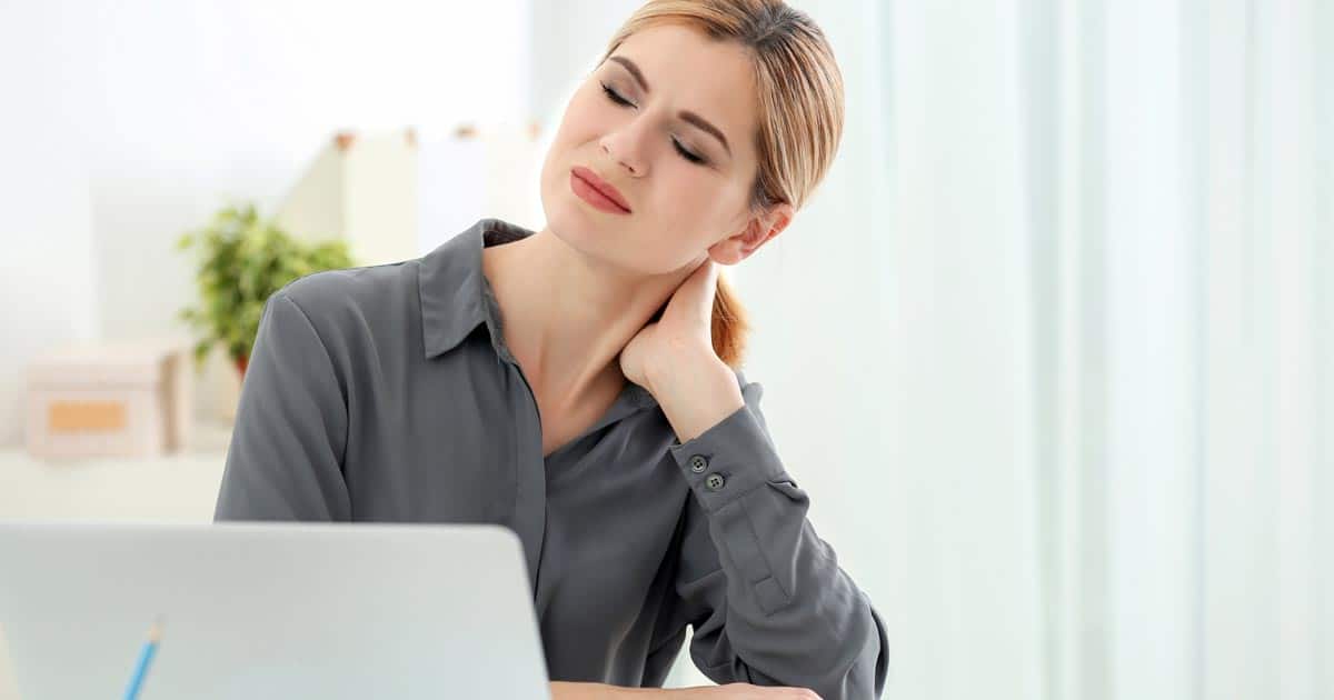 A woman is sitting in front of her laptop touching her neck.