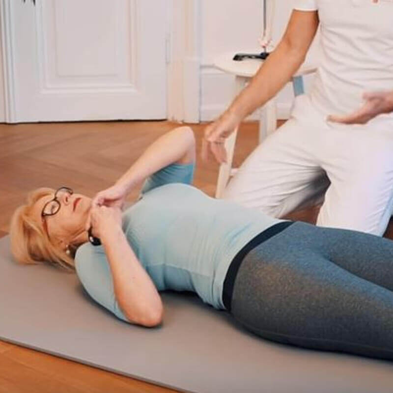 Woman performing a fascia roll massage on the floor, using a fascia ball to massage her shoulder joint.