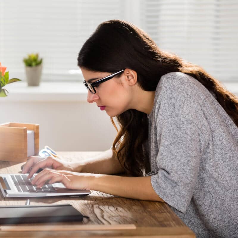A woman is bent over a laptop working.