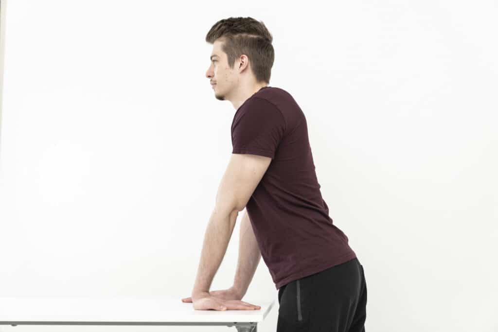 A man is placing his palms on a table to stretch his arms.