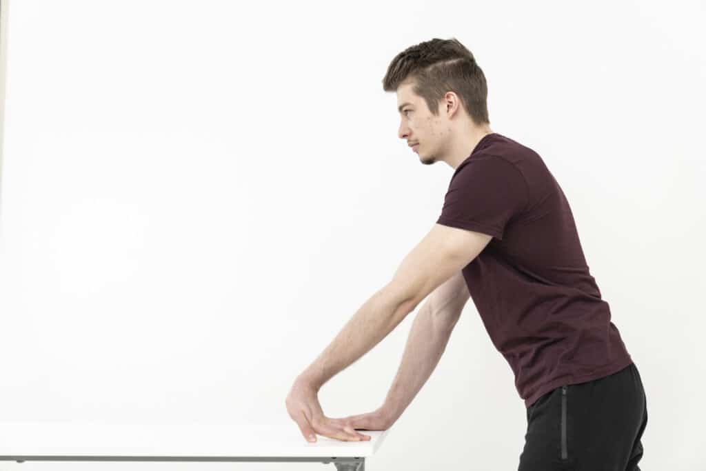 A man is stretching his arms using a table.
