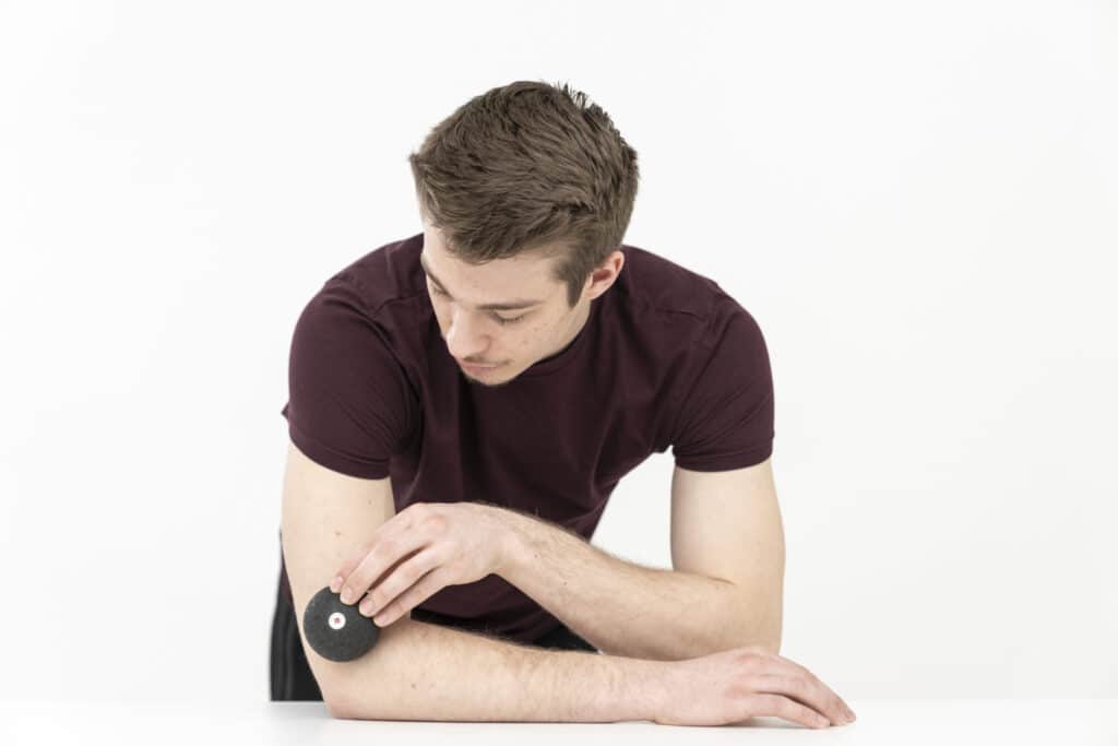 A man is foam rolling his elbow with a massage ball.