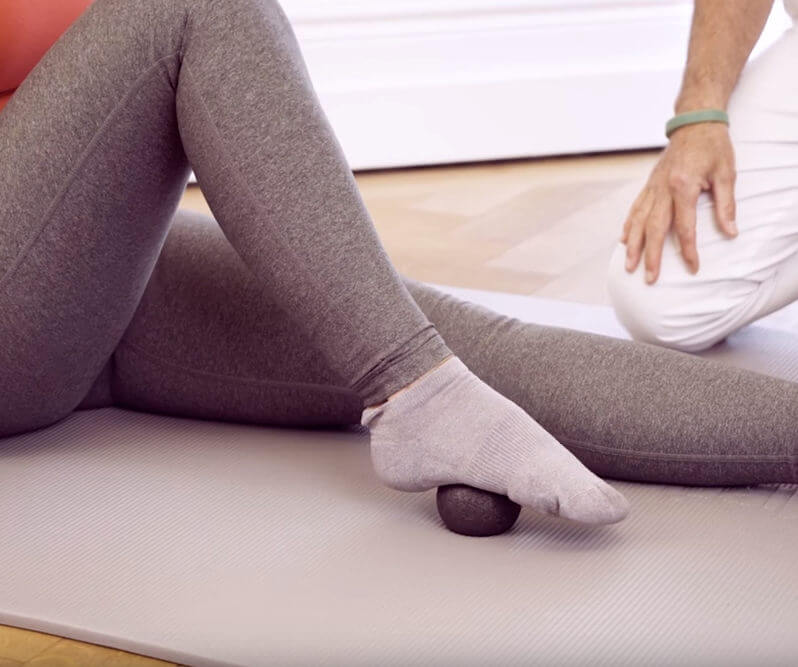 A woman is massaging her feet with a mini massage ball.