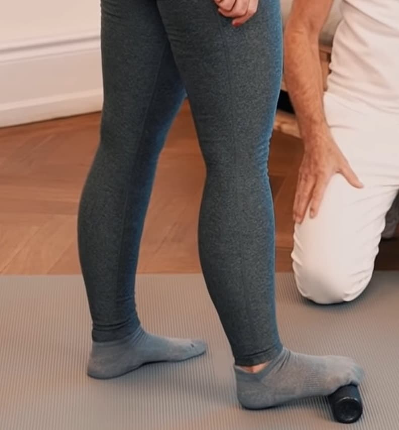 A woman is massaging her heel with a foam roller.