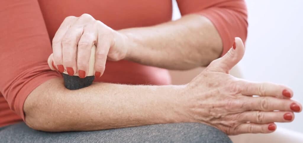 A woman is using a Pain Releaser tool to press her elbow