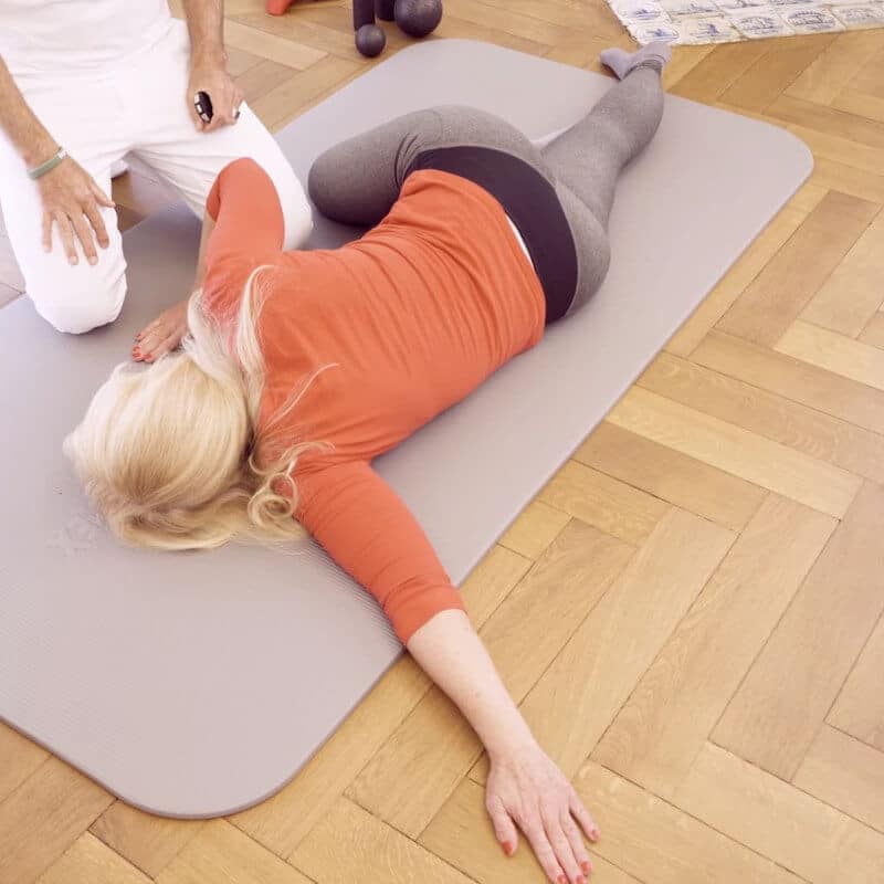 A woman is lying on a mat, one arm stretched out and the other angled and propped up.
