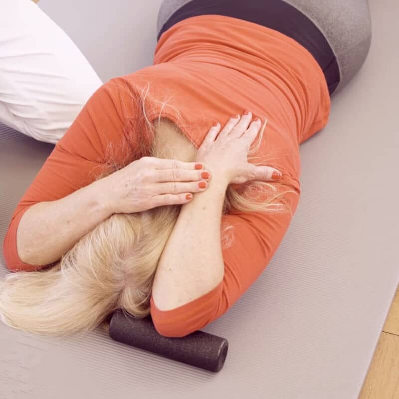A woman is on the floor, bending back her elbow to stretch it.