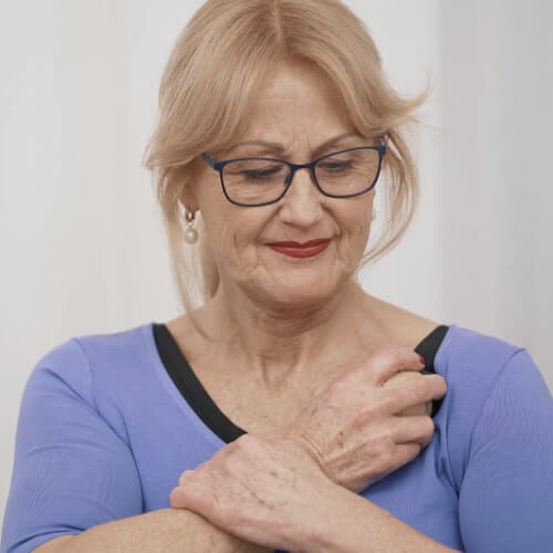 A woman is osteopressing herself to treat her frozen shoulder.