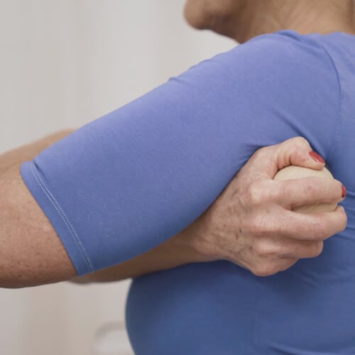 A woman is pressing a point below her shoulder to relieve her shoulder pain.