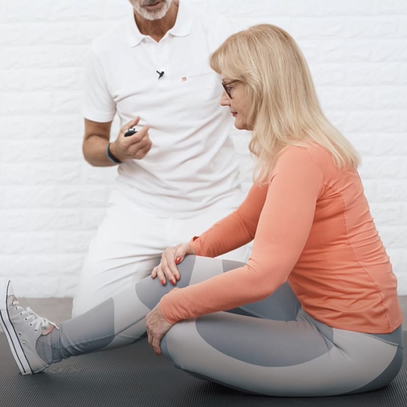 Ina sits on the ground with her left leg bent and her foot placed under her right straightened leg. Her hands touch her knees.
