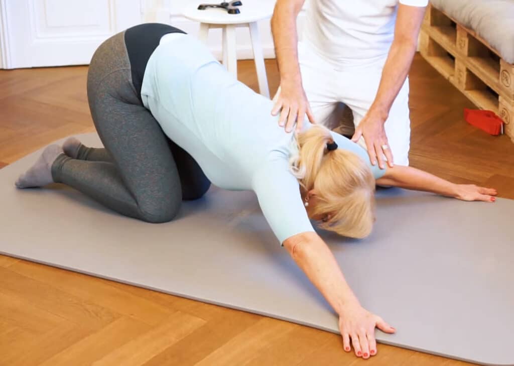 A woman is kneeling on a mat, her arms stretched apart.