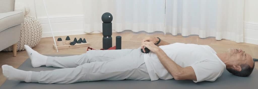 Roland is lying on a mat, massaging himself with a massage ball.