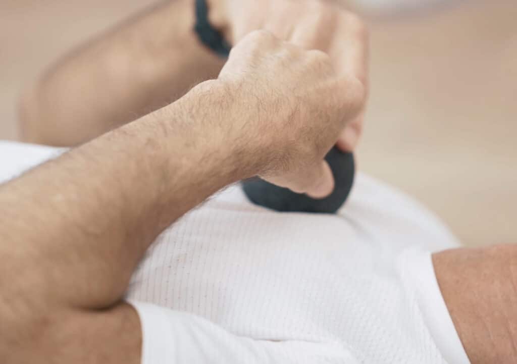 Two hands hold a massage ball that is pressed into a chest. The person wears a white shirt.