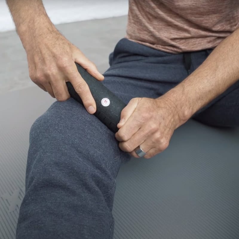 A mini foam roller is pressed into a right thigh. The person sits on a mat. Trunk, right thigh and forearms are visible.