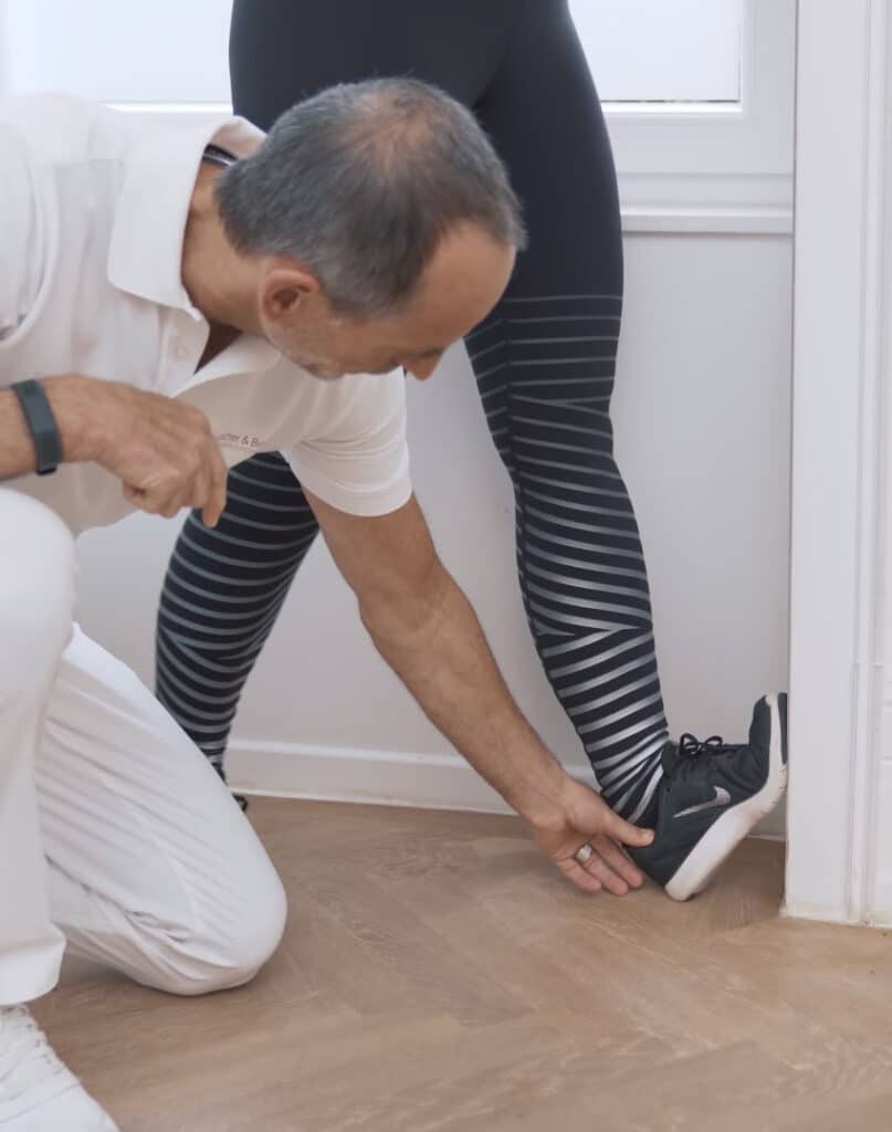 A woman is using a door frame to stretch her knees.