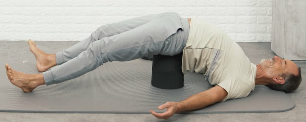 Roland lies on the ground. A black stack is placed unter his sacrum and lift up the buttock. Shoulders, head, arms and feet touch the floor.