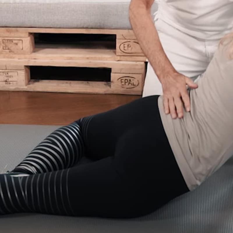 A woman is letting her pelvis hang towards the floor, a man's hand is on her back.