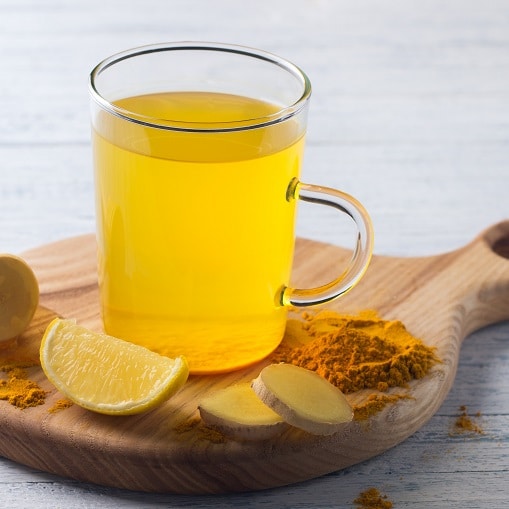 image of glass filled with tea containing honey, lemon, ginger and turmeric