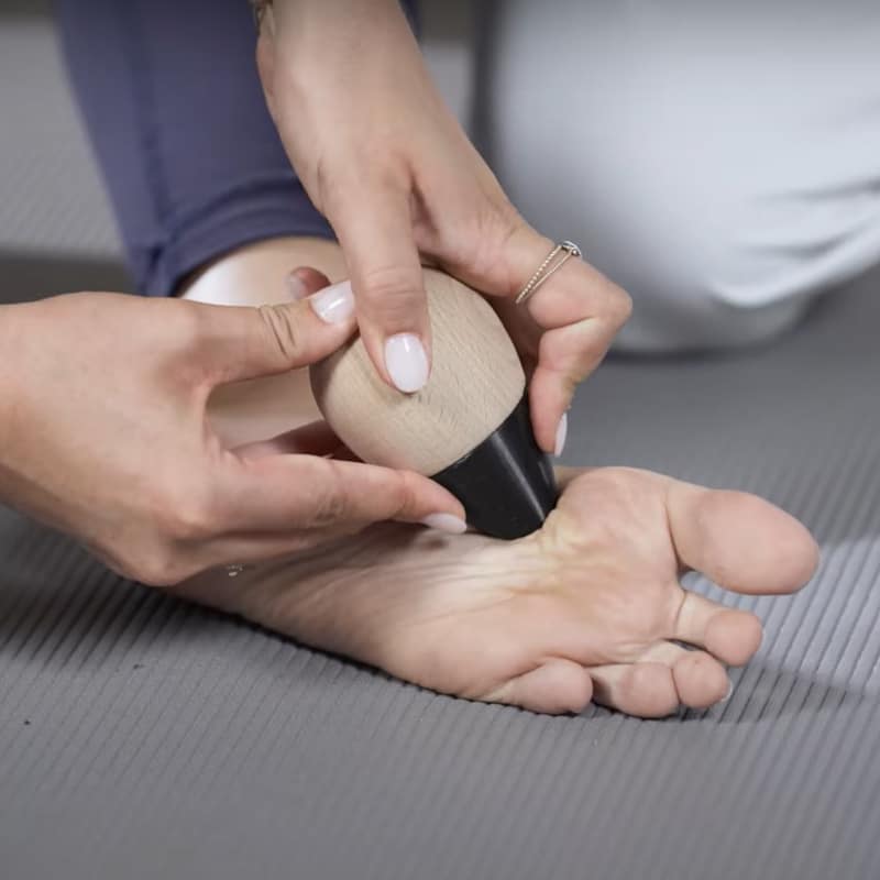 A woman is pressing the Osteopressure tool into the ball of her foot.