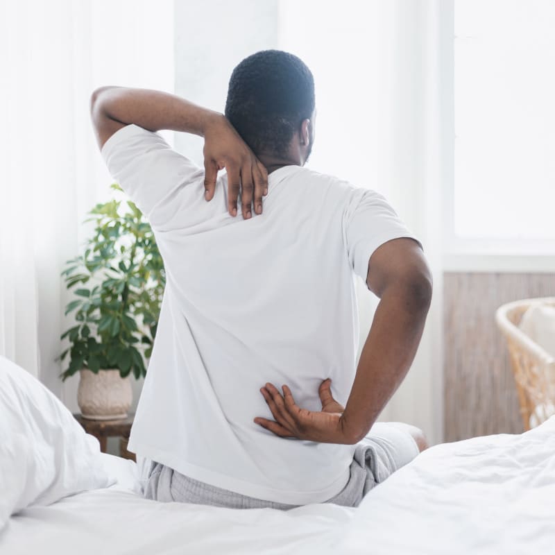 A gentleman with ankylosing spondylitis is sitting on his bed.