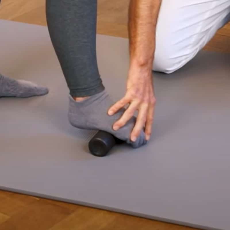 A woman is standing with a massage roller under her right foot..