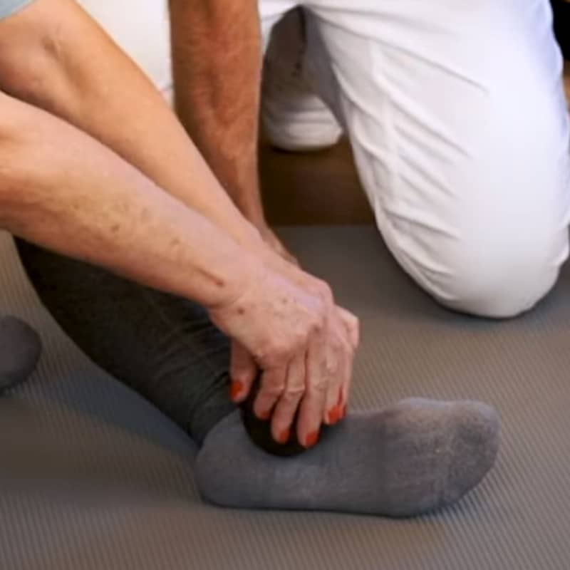 A woman is massaging her foot with a massage ball.