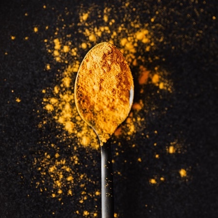 A heaped spoon containing a yellow spice which is called turmeric.