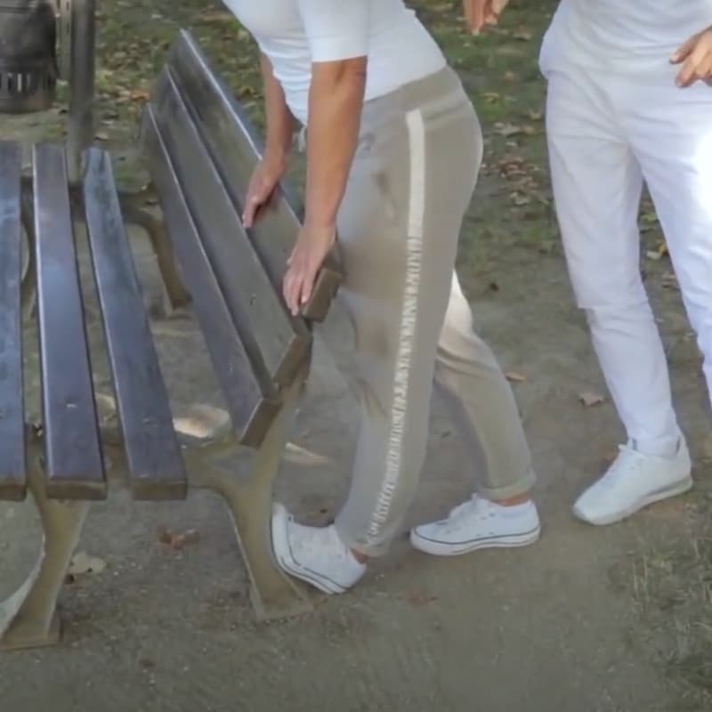Ina is stretching her foot against a park bench.