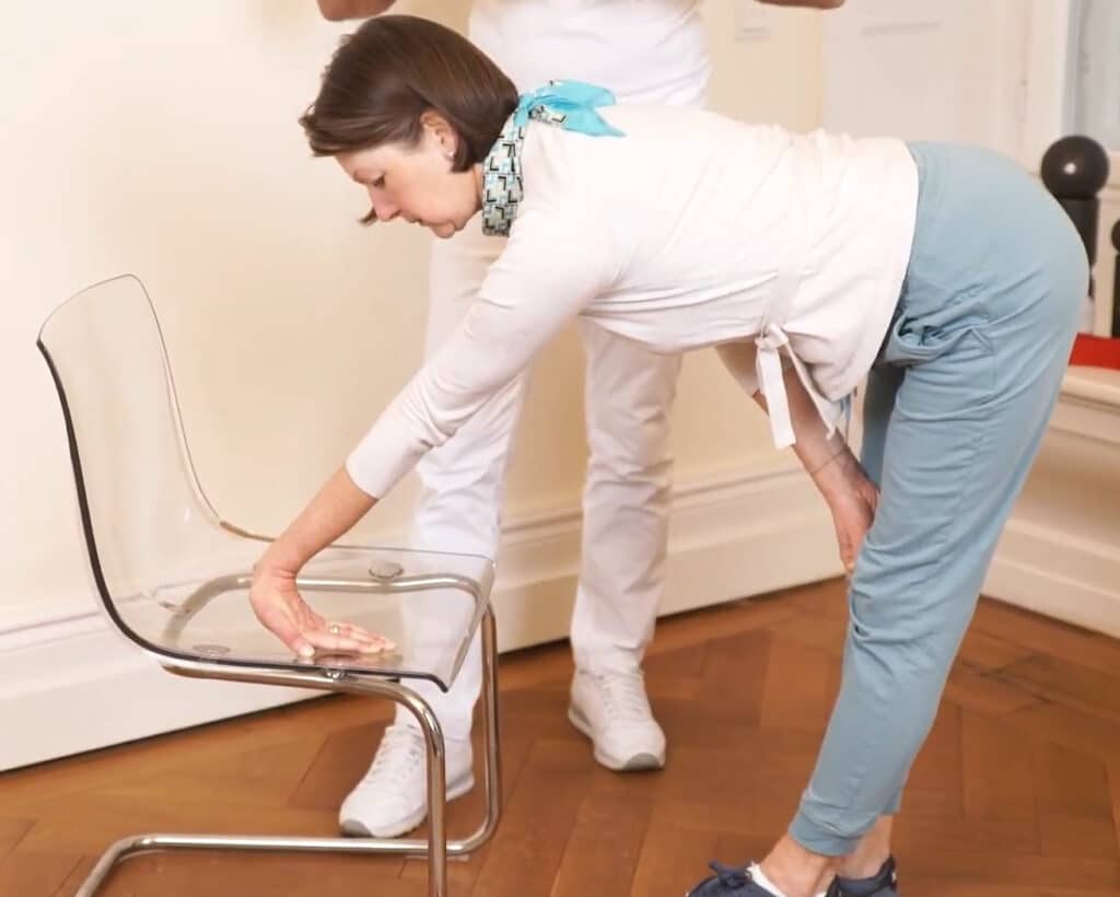 A woman is stretching her wrist: her palm rests on a chair, the wrist lifted up.