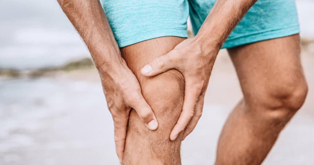 A man is holding his hurting knee. His patellar tendon is inflamed.