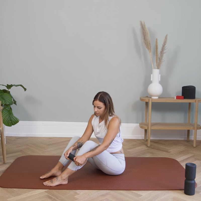 A woman is foam rolling her shin with a Liebscher & Bracht Mini Foam Roller.