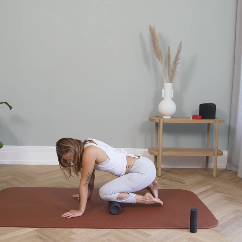 A woman is foam rolling her shin with a Liebscher & Bracht Midi Foam Roller.