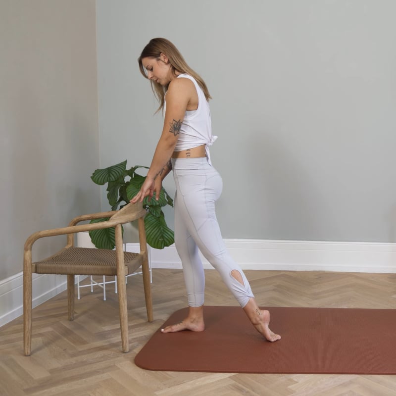A woman is standing behind a chair stretching her shin.