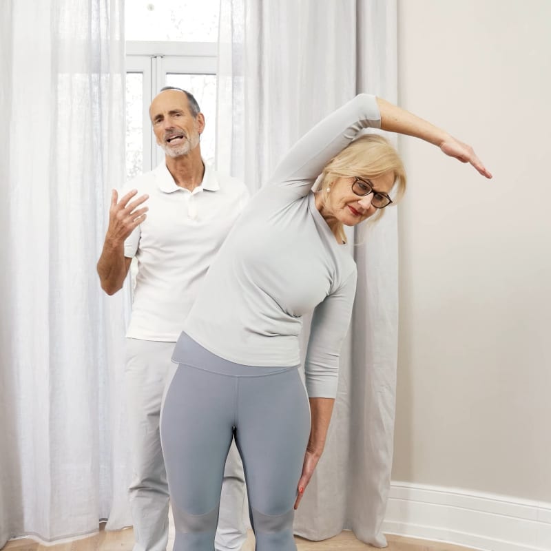 Ina is reaching her right hand over her head and bending her upper body to the left.