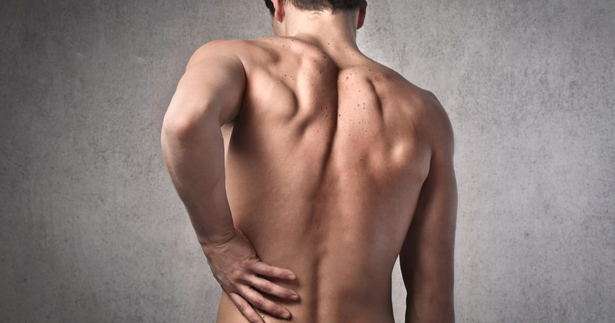A man with lumbar spinal stenosis is touching his back.