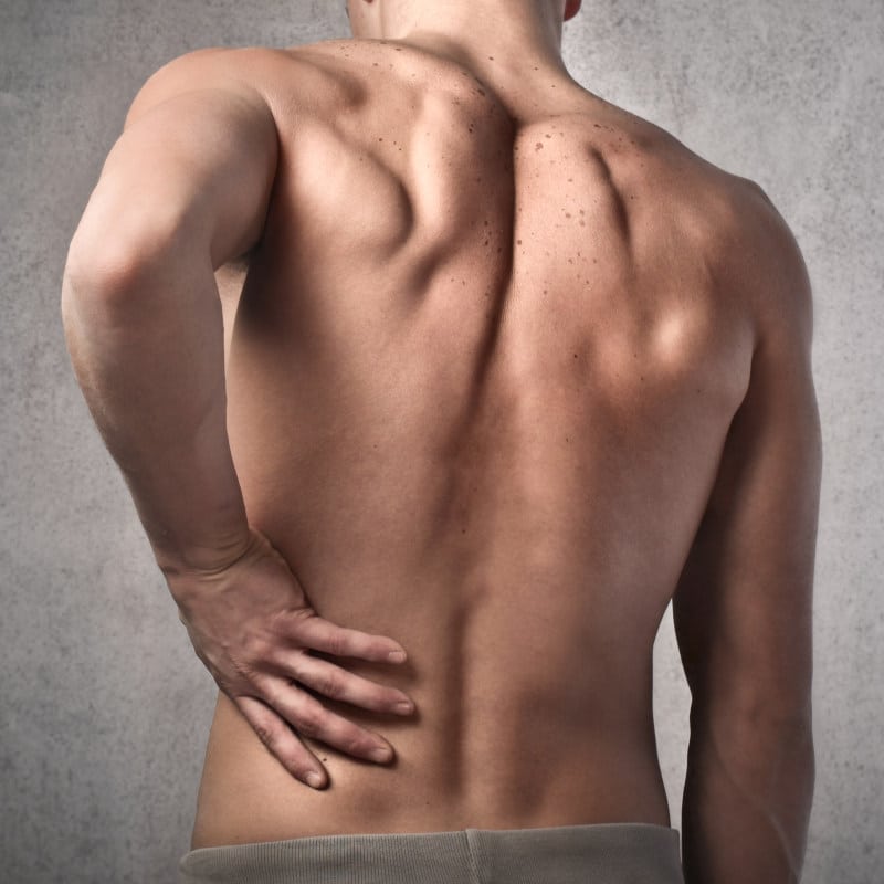 A man with lumbar spinal stenosis is touching his back.