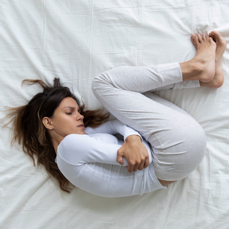 A woman who has fibromyalgia is lying in bed in the fetal position.