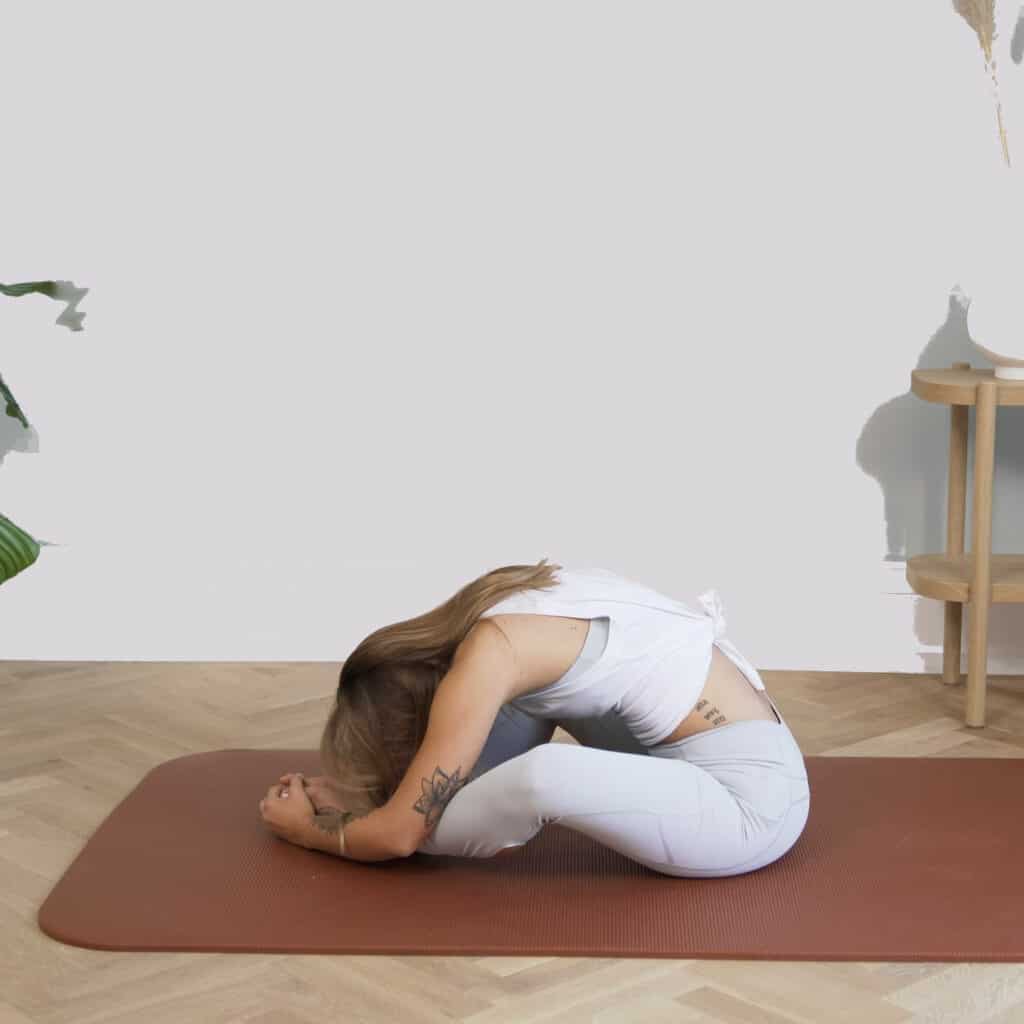 A girl is sitting on the floor leaning into her ankles.