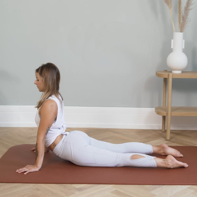 A girl is lying on the floor. She's propped up on her hands stretching her pelvis.