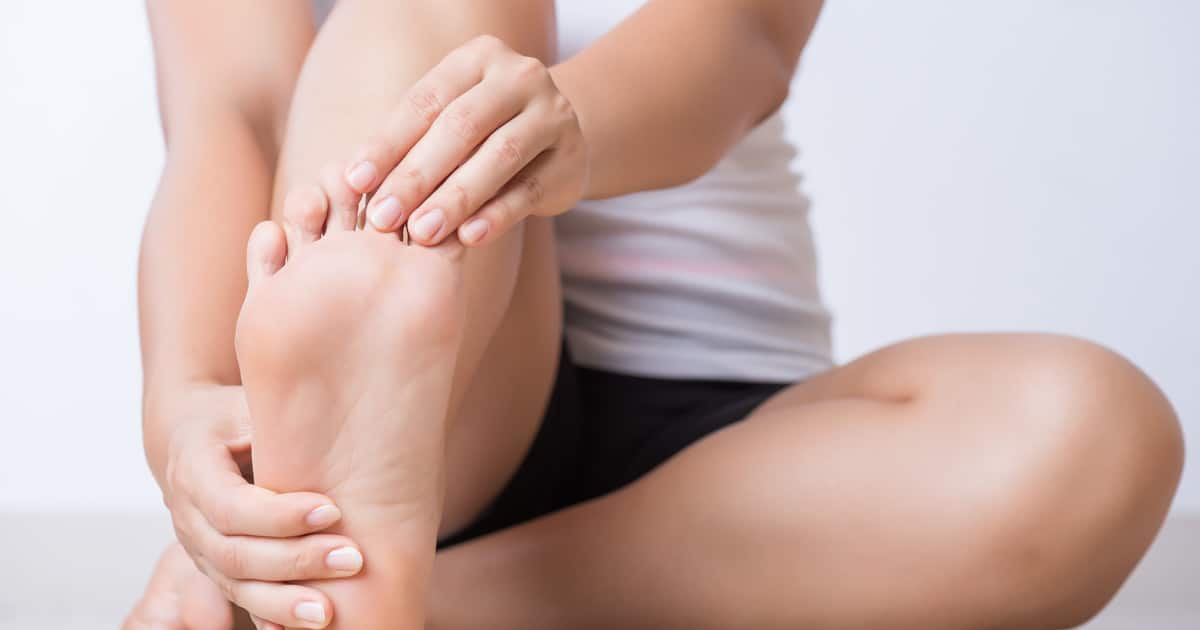 A woman is stretching her right foot. She's pulling her toes back with one hand and grabbing her ankle with the other.