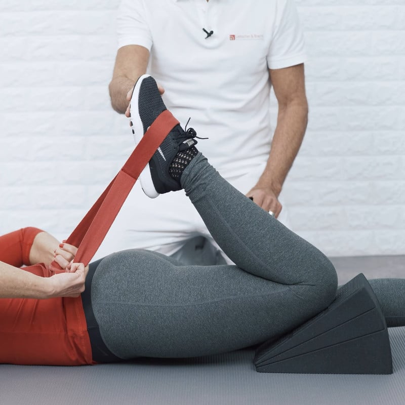 Ina is resting her thigh on The Knee Hero. She has The Stretching Strap around the bridge of her foot and is pulling it toward her buttocks.