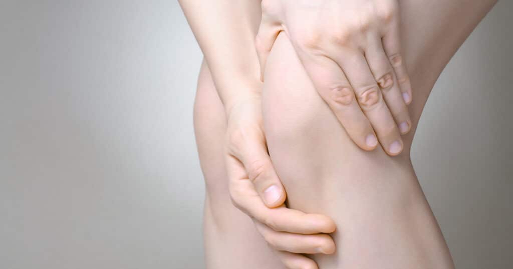 A woman is clutching her knee because it hurts.
