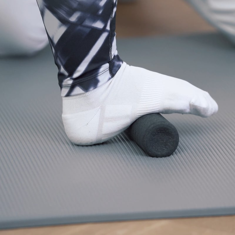 A woman is rolling her foot along the mini foam roller.