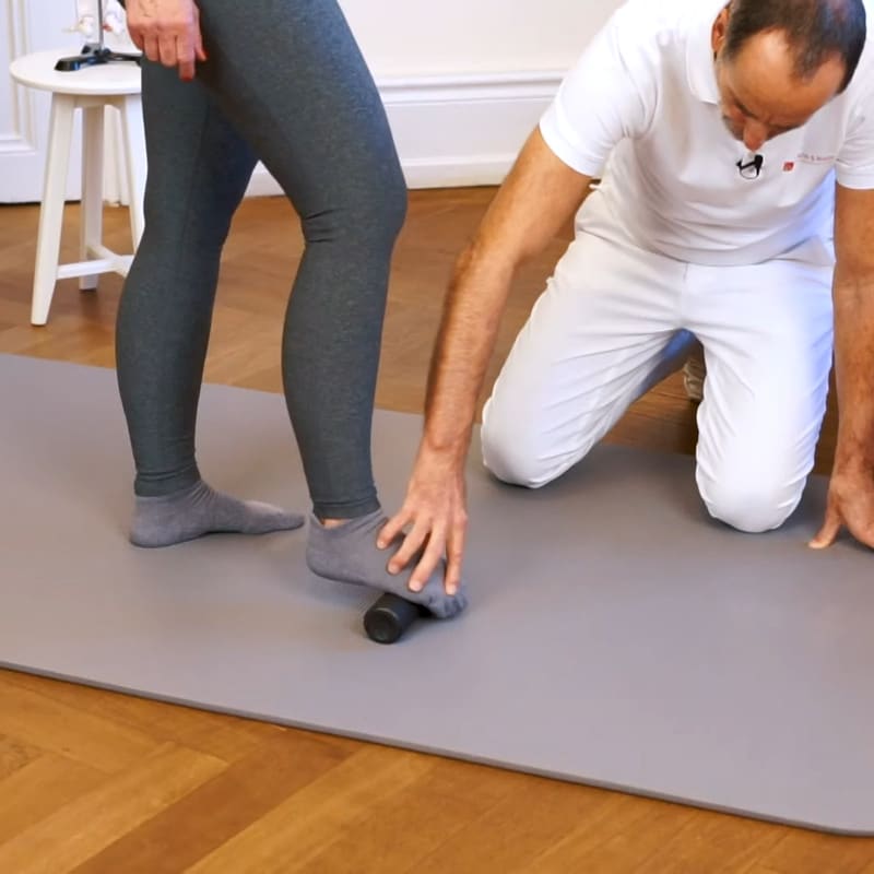 A woman is standing on the Mini Foam Roller with her right foot, Roland Liebscher-Bracht is touching her foot.