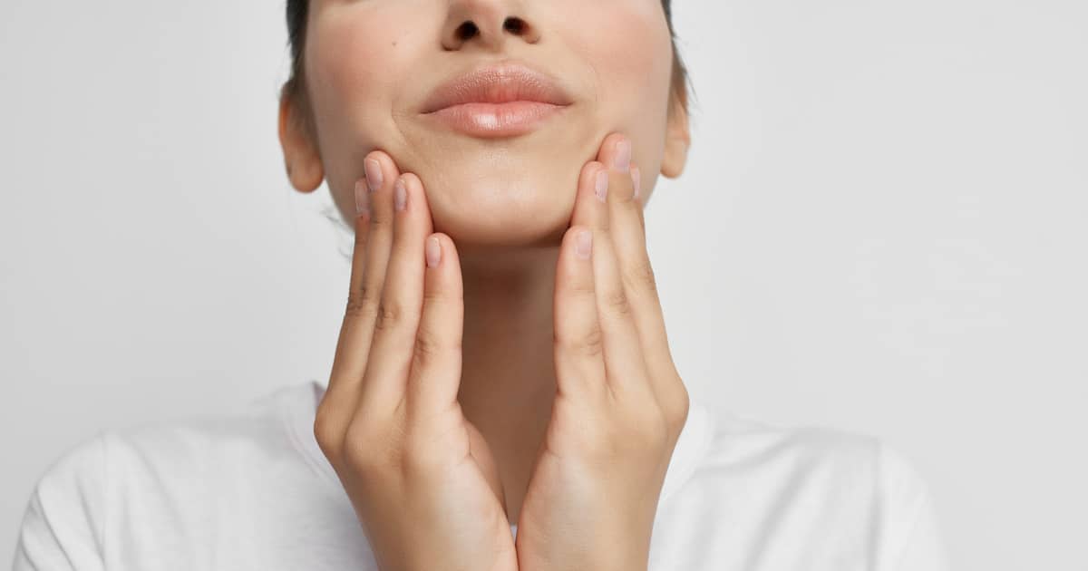 Closeup of a woman touching her jaw.