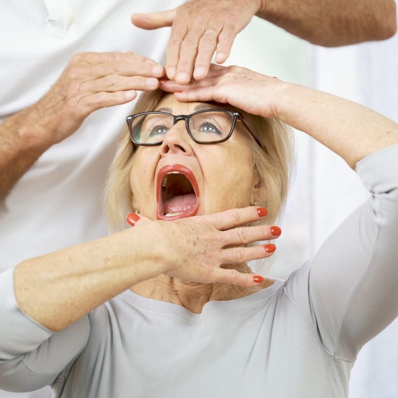 A woman is pulling her chin down with one hand and pushing her forehead back with the other.