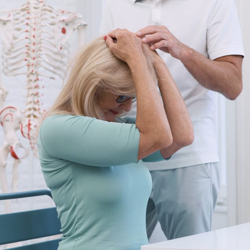 A woman has both hands on the crown of her head and she's pulling her head forward. Roland Liebscher-Bracht is touching her head with his left hand.