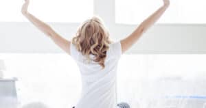 A woman is sitting on a bed and stretching her arms to both sides.