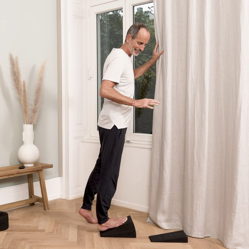 Roland Liebscher-Bracht is standing on The Knee Hero stretching his calf.